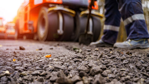 Eine unfertige Straße, Bauarbeiter und Maschinen im Hintergrund