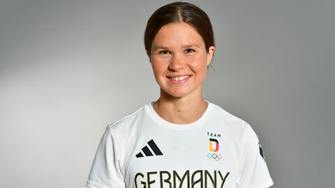 Junge Frau mit braunen Haaren lächelt in die Kamera. Sie trägt ein weißes Trikot auf dem "Germany" steht.