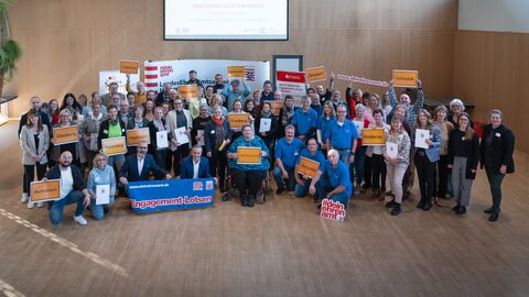 Viele Menschen stehen zusammen und schauen in die Kamera. Einige halten Ortsschilder auf denen hessische Orte stehen